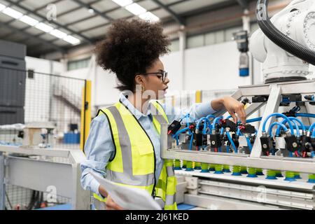 Engineer holding blueprint examining robotic arm machine in factory Stock Photo