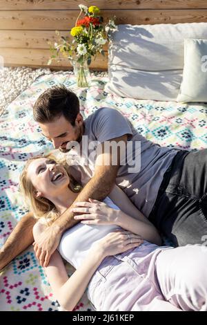 Man looking at girlfriend lying down on picnic blanket at terrace Stock Photo