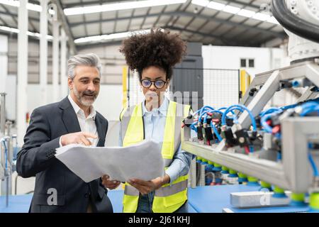 Businessman discussing over blueprint with engineer in factory Stock Photo