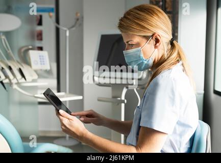 Dentist with protective face mask using tablet PC at dental clinic Stock Photo