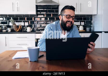 Happy freelancer with laptop using smart phone at home Stock Photo
