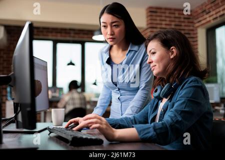 Creative designers developing digital arts on PC while discussing about 3D technology. Professional office workers pointing out wrong blueprint of project while using work computer. Stock Photo