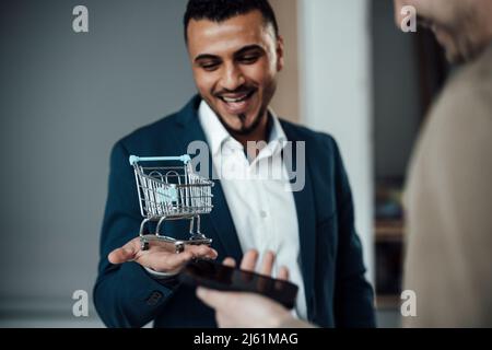 Happy businessman showing shopping cart model to colleague at office Stock Photo