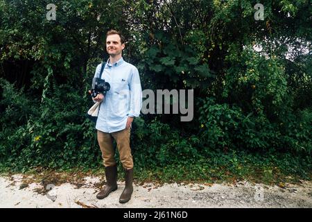 Smiling man holding vintage medium format camera standing with hand in pocket at park Stock Photo