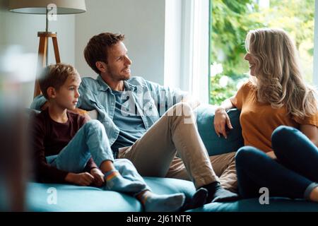 Man talking with woman sitting by son on sofa at home Stock Photo