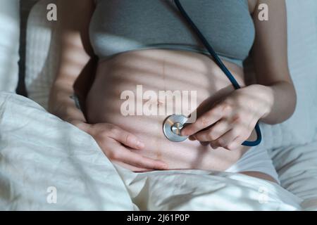 Pregnant woman listens to the baby heartbeat and movements with a stethoscope or fetoscope or Pinard Horn. Prenatal fetal health, anxiety, fear concept. High quality photo Stock Photo