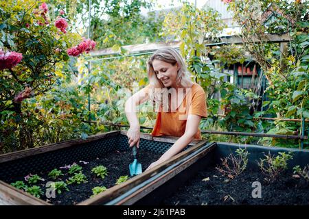 Smiling blond woman with shovel gardening in backyard Stock Photo