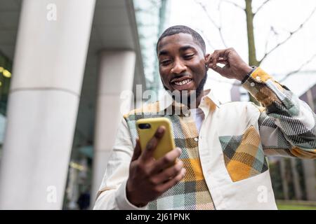 Smiling man wearing wireless in-ear headphones having video call on mobile phone Stock Photo