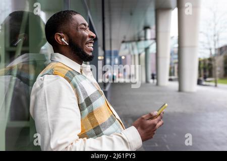 Happy man with eyes closed holding mobile phone leaning on glass wall Stock Photo