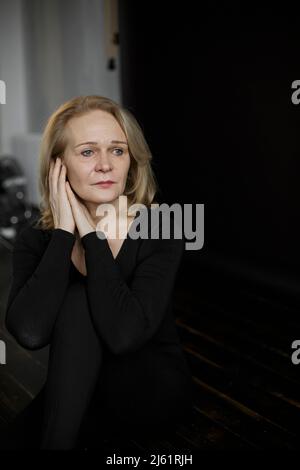 Thoughtful sad woman in black bodysuit sitting on floor at home Stock Photo