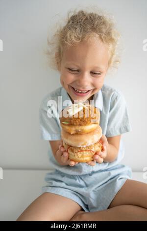 Smiling girl holding stack of doughnuts sitting on table Stock Photo