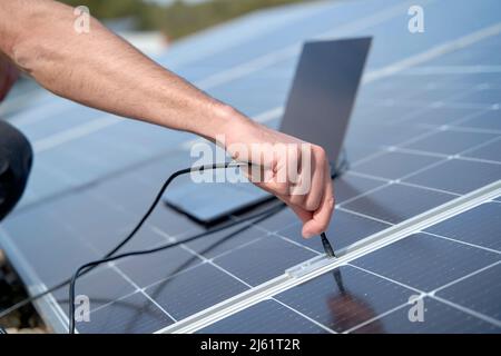 Engineer plugging in power supply cable charger of laptop to solar panels Stock Photo