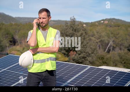Engineer talking on mobile phone standing by solar panels Stock Photo