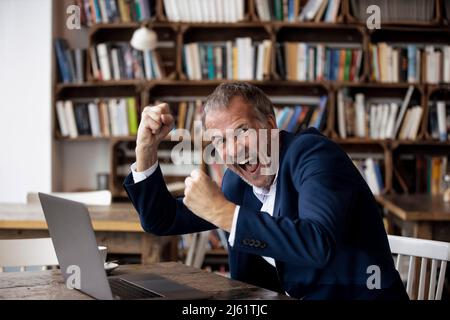Excited businessman sitting with laptop at table celebrating in cafe Stock Photo