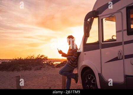 Man leaning on camper van and using smart phone Stock Photo