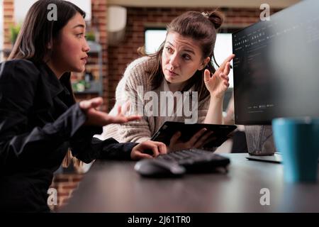 Unsure asian programming expert asking colleague about generated bug report file. Blockchain developing engineer using high technology software to defend database system. Stock Photo