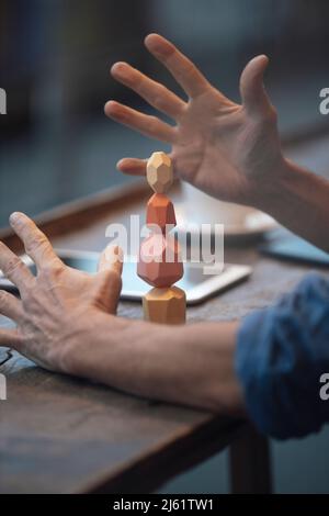 Businessman balancing stack of stones on wooden table at cafe Stock Photo
