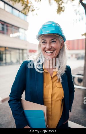 Cheerful engineer wearing with clipboard standing at office park Stock Photo
