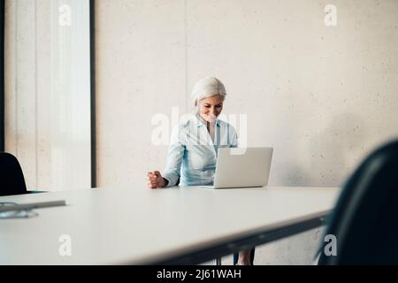 Smiling working woman using laptop sitting at desk in office Stock Photo