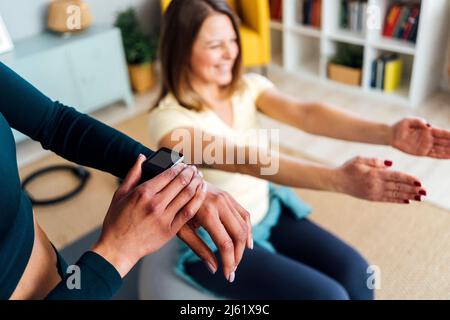 Woman adjusting smart watch by friend working out at home Stock Photo
