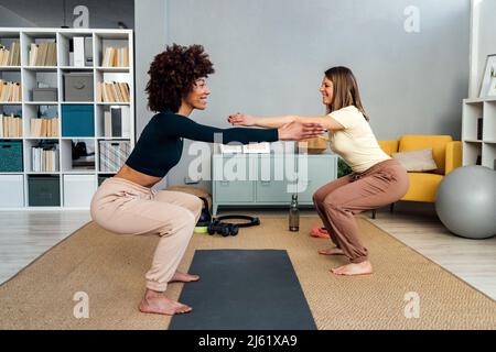 Smiling friends doing squats together in living room at home Stock Photo