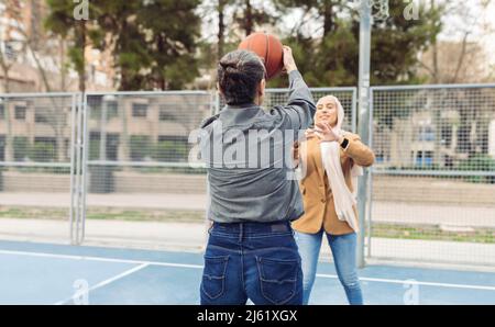 Businesswoman playing basketball with young colleague at sports court Stock Photo