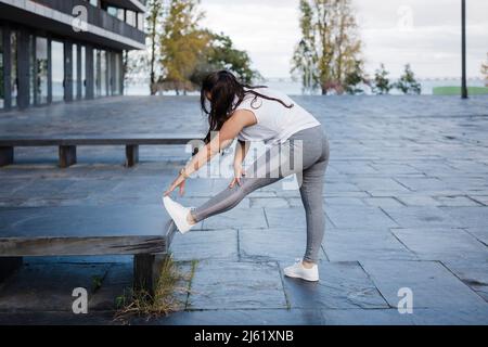 Woman doing stretching leg exercise by concrete seat Stock Photo