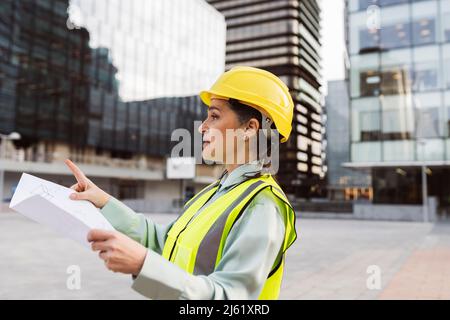 Engineer wearing hardhat holding blueprint working outside modern building Stock Photo