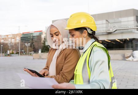 Young businesswoman sharing tablet PC with architect wearing hardhat Stock Photo