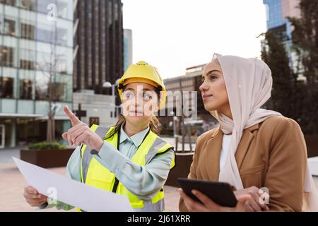 Engineer wearing hardhat discussing with businesswoman holding tablet PC Stock Photo