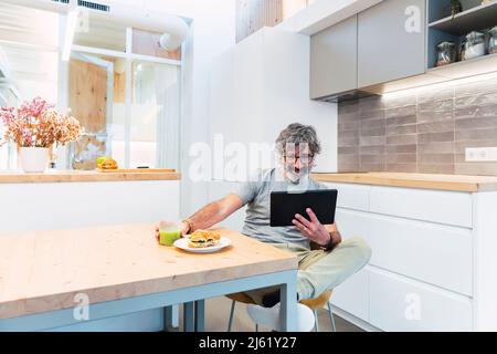 Man sitting at table using tablet PC and having breakfast at home Stock Photo
