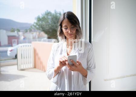 Pregnant woman in sports bra using smart phone in doorway at home