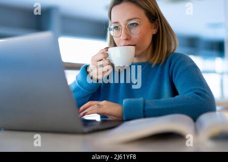 Young woman drinking coffee and using laptop at table Stock Photo