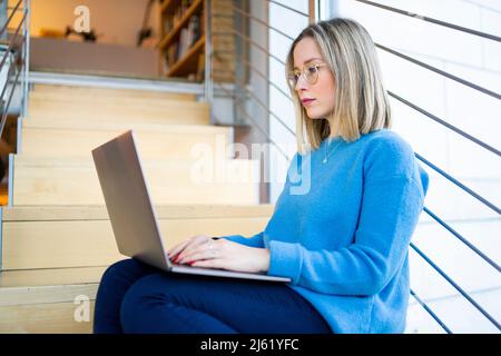 Young woman using laptop sitting on staircase Stock Photo