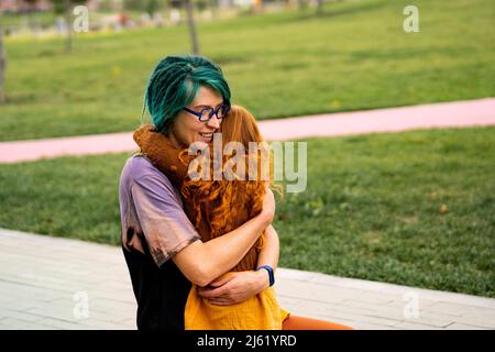 Smiling mother hugging daughter in public park Stock Photo