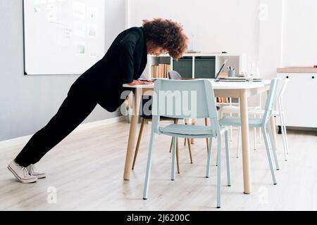 Businesswoman doing push-ups on desk in office Stock Photo