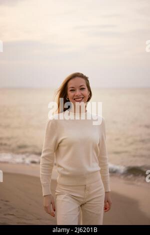 Smiling woman standing on beach in front of Baltic sea at sunset Stock Photo