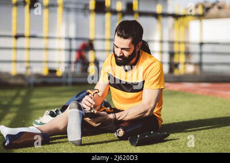 Bearded man adjusting prosthetic leg with screwdriver sitting on grass Stock Photo