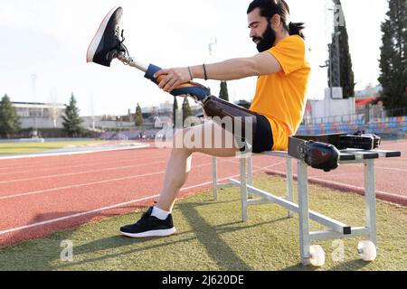 Bearded man removing prosthetic leg sitting on bench Stock Photo
