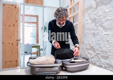 Senior freelancer packing suitcase in bedroom at home Stock Photo