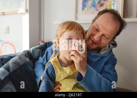 Father helping daughter using asthma inhaler sitting at home Stock Photo
