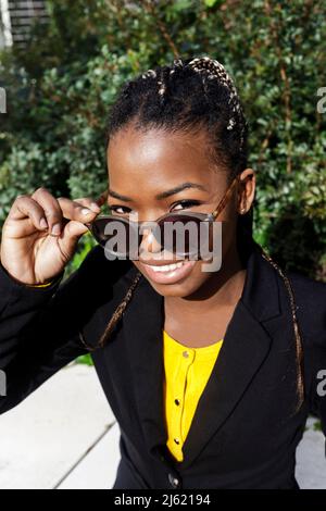 Happy young woman braided hair holding sunglasses on sunny day Stock Photo