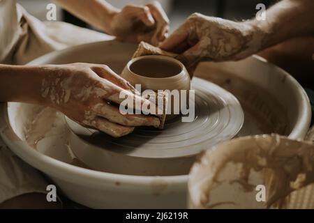 Woman with young man shaping bowl on potter's wheel in workshop Stock Photo