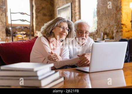 Smiling senior couple looking at laptop sitting on sofa in boutique hotel Stock Photo