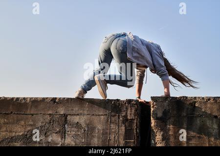 Young woman jumping over concrete wall, rear view Stock Photo