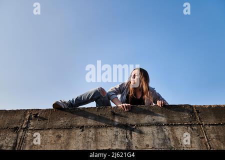 Young woman climbing over concrete wall Stock Photo