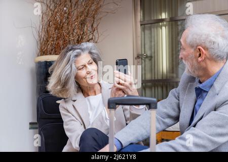 Smiling senior woman photographing man through mobile phone Stock Photo