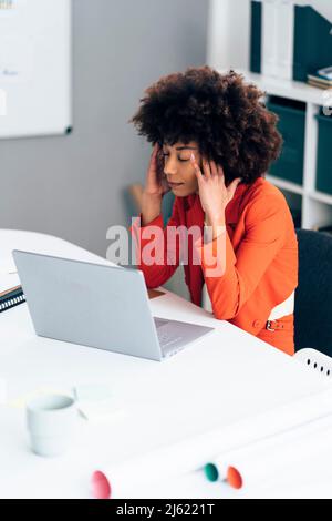 Stressed businesswoman with head in hands sitting with laptop at desk Stock Photo