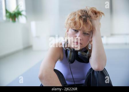 Young woman wearing headphones sitting with hand in hair Stock Photo