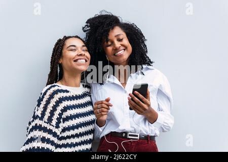 Happy colleagues with eyes closed enjoying music through in-ear headphones standing by wall Stock Photo